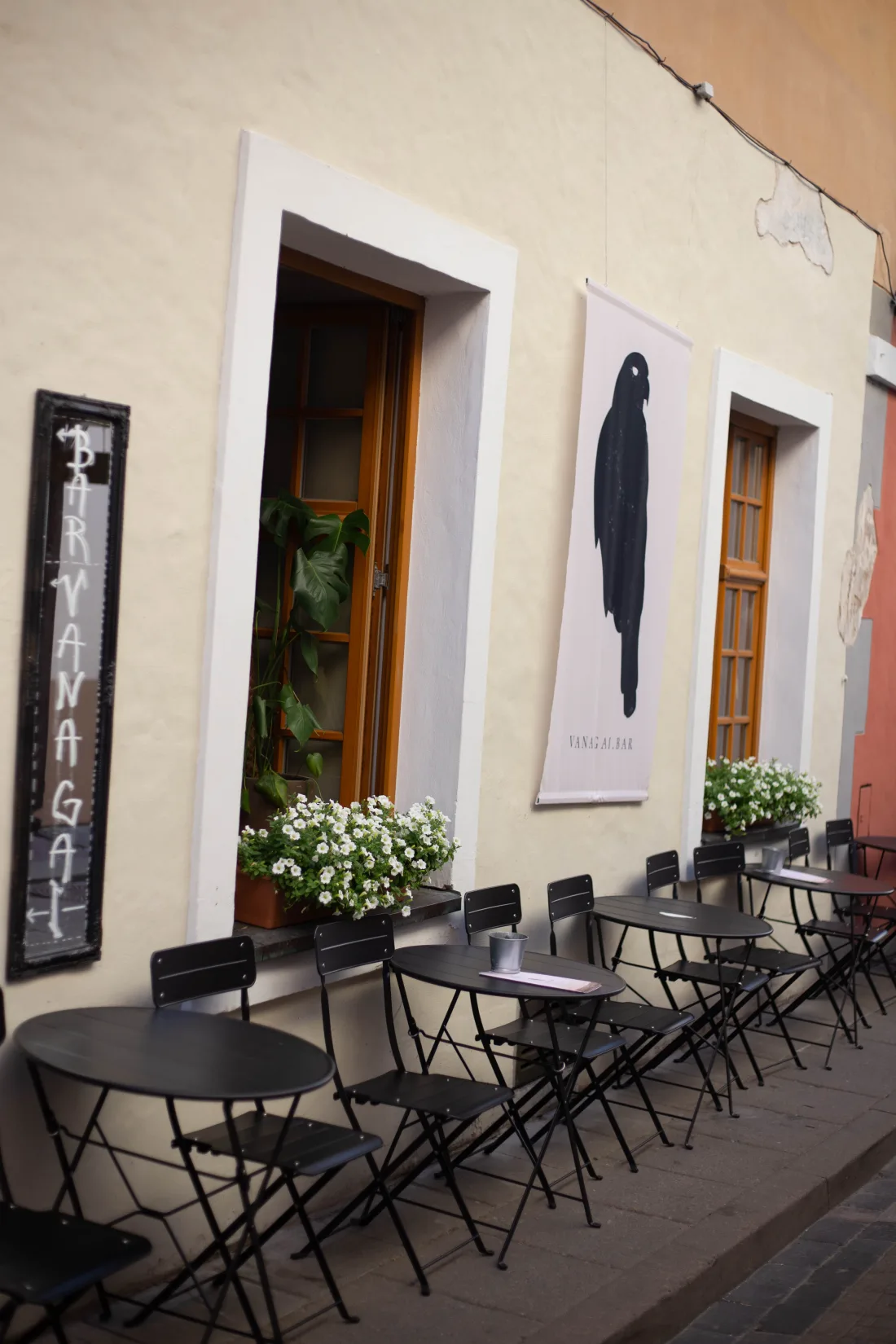 Vanagai's terrace tables and chairs on the cobblestones of Stiklių gatvė, beside the bar's hawk banner