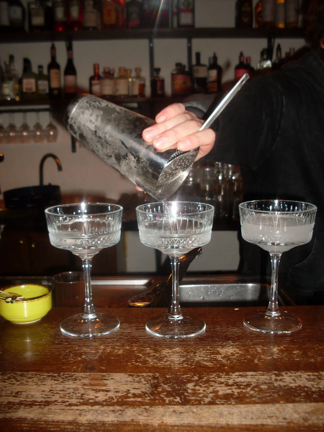 A bartender straining three coupe cocktails over the bar at Vanagai, a cocktail bar on Stiklių gatvė in Vilnius Old Town